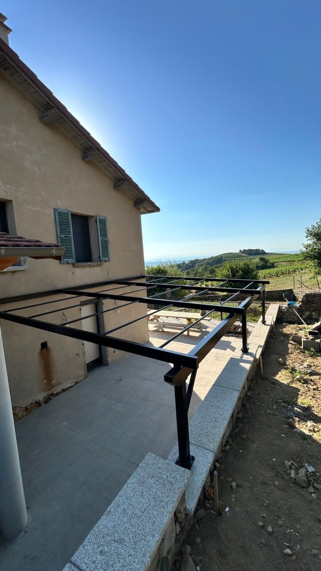 Ossature de pergola m&eacute;tallique noire fabriqu&eacute;e sur mesure et fix&eacute;e &agrave; la fa&ccedil;ade d&rsquo;une maison &agrave; Limony