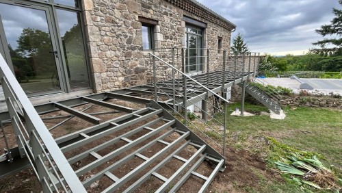 Structure de terrasse métallique avec escaliers et garde-corps devant une maison en pierre à Peaugres